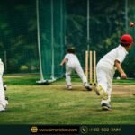 Young cricket player in full gear practicing batting at an AIM Cricket Academy net session with a coach.