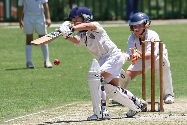 Young cricketer playing a front foot shot during a match with wicketkeeper behind the stumps